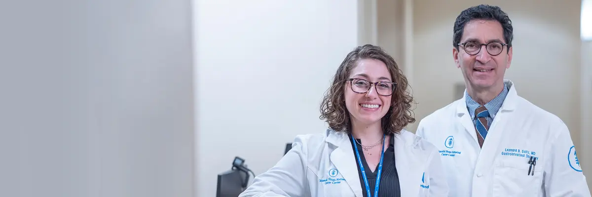 MSK colon cancer experts clinical nurse Marissa Gelfand and gastrointestinal medical oncologist Dr. Leonard Saltz, wearing white coats, are standing together.   
