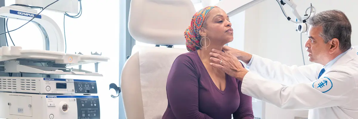 During an exam, head and neck surgeon Dr. Snehal G. Patel sits next to is patient with his hand on her neck. 