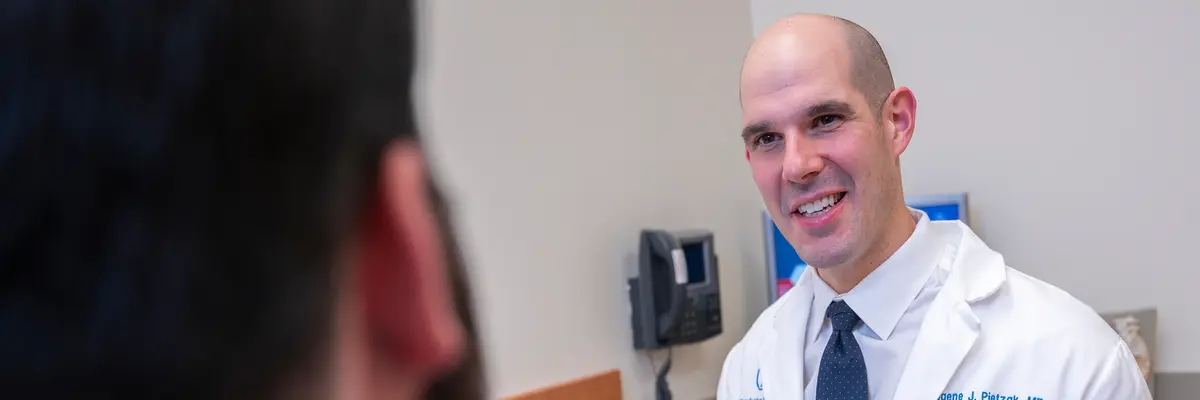 Urologic surgeon Dr. Eugene Pietzak, wearing a white doctors’ coat, talks with his patient in an MSK exam room. 