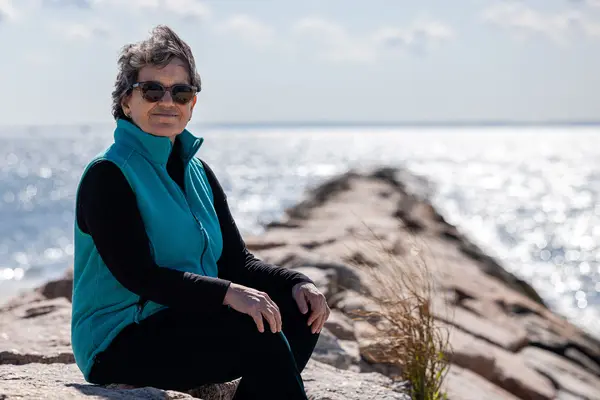 Joanna, sitting on rocks by water, was able to afford cancer care at MSK, which accepts most insurance plans.    