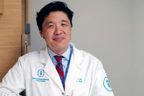 Medical oncologist Dr. Alan Ho, in a white doctors’ coat, treats people with head and neck cancer at MSK in New York City. 