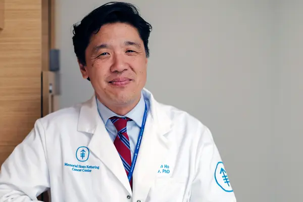 Medical oncologist Dr. Alan Ho, in a white doctors’ coat, treats people with head and neck cancer at MSK in New York City. 