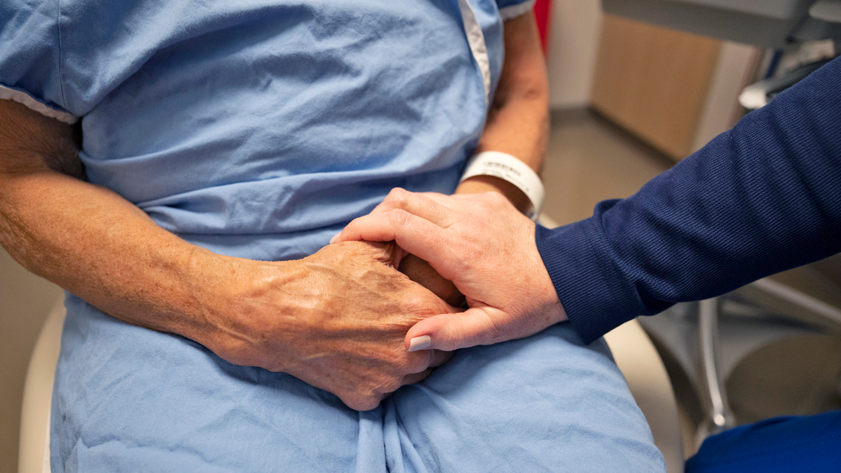 A person placing their hand on a patient’s hand to comfort them. 