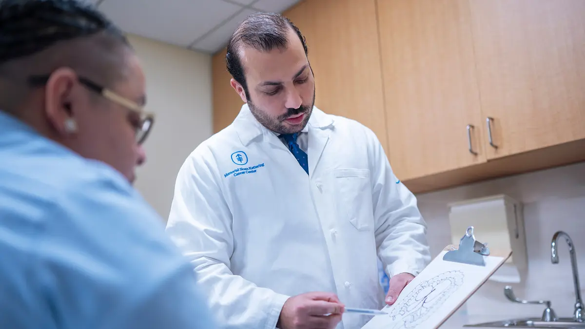 In an exam room, MSK colorectal surgeon Dr. Mohammad Ali Abbass points to a clipboard while talking with his MSK patient.  