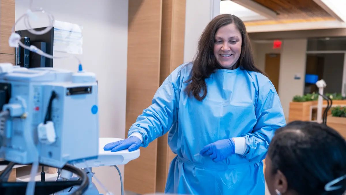 MSK nurse Elisa Goldberg, wearing scrubs, talks to a patient in an infusion suite at the David H. Koch Center for Cancer Care. 