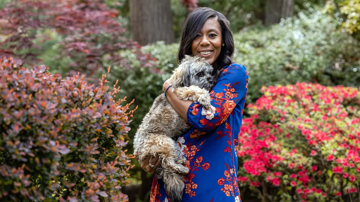 Rectal cancer survivor Roxanne Joseph, who was treated at MSK, is standing by colorful bushes and holding her dog.  