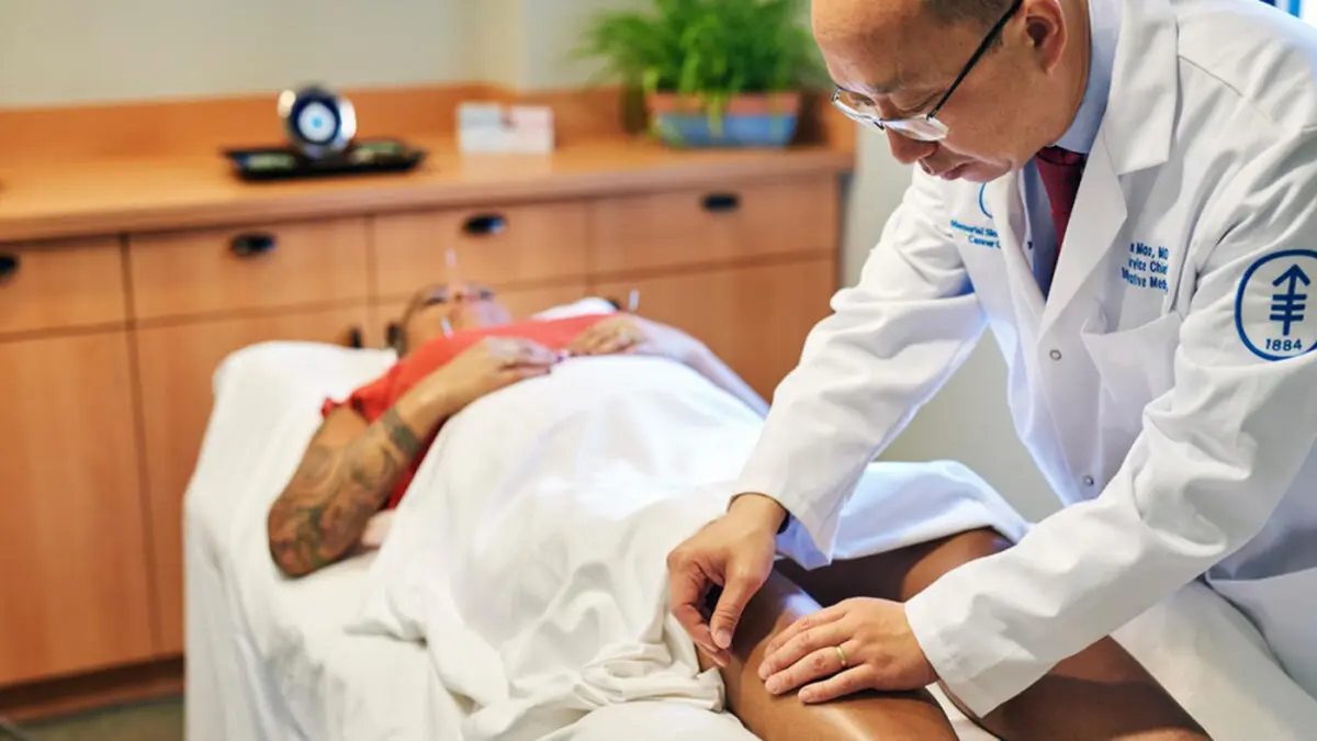 Dr. Jun Mao is treating an MSK patient, lying on a table, with acupuncture. 