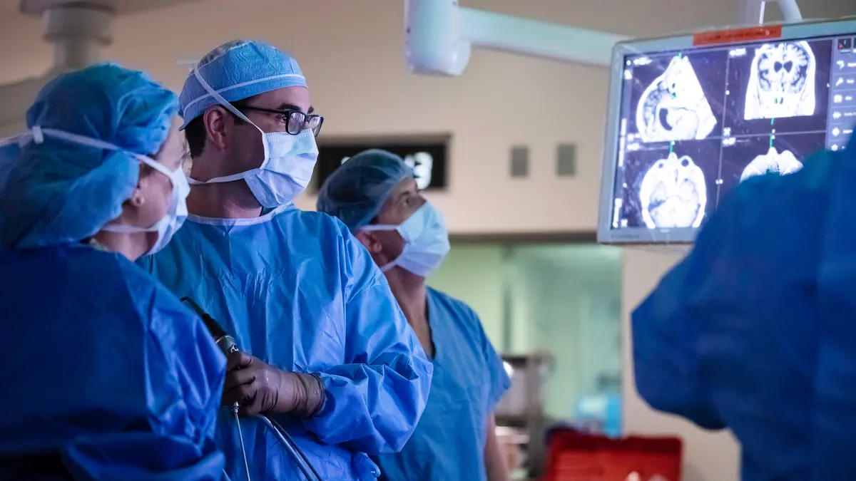 Head and neck surgeon Dr. Marc Cohen and 3 members of the MSK surgery team, all dressed in surgical scrubs, look at a head scan on a monitor. 