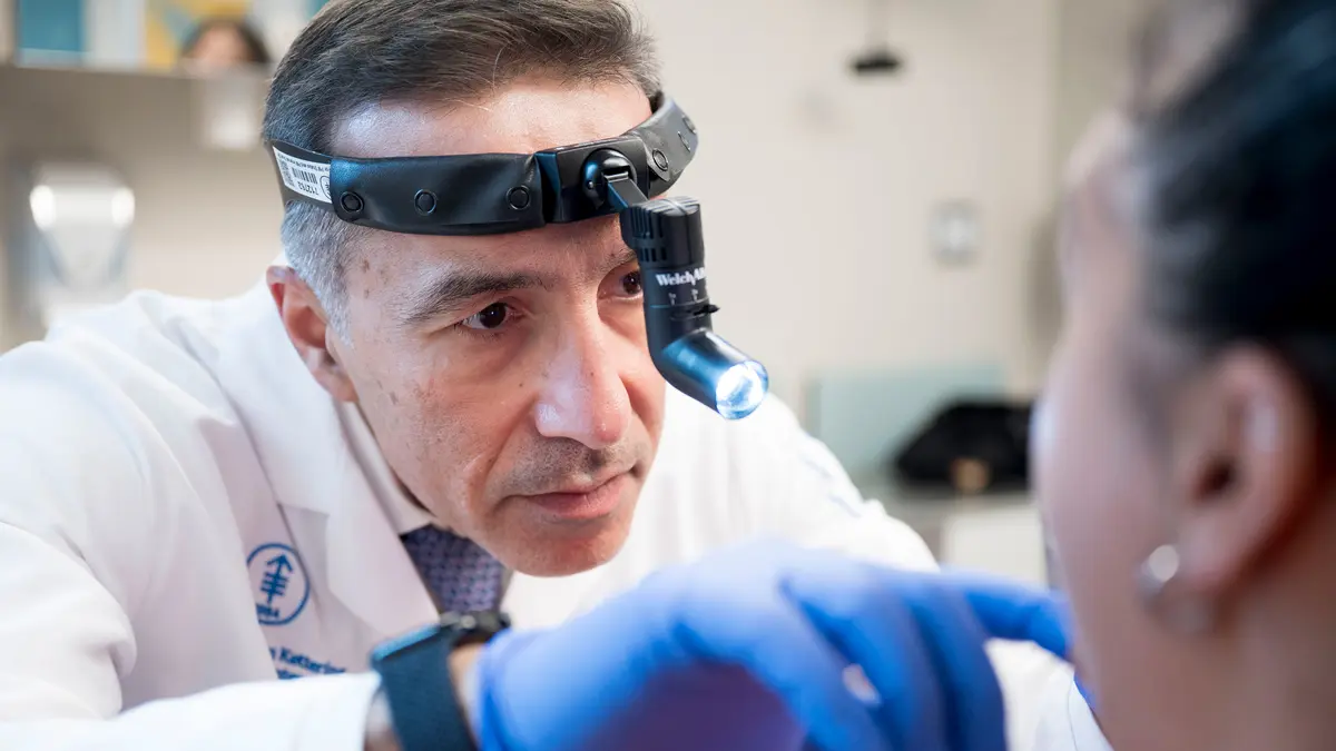 Head and neck surgeon Dr. Babak Givi, wearing a medical headlamp, examines a patient. 