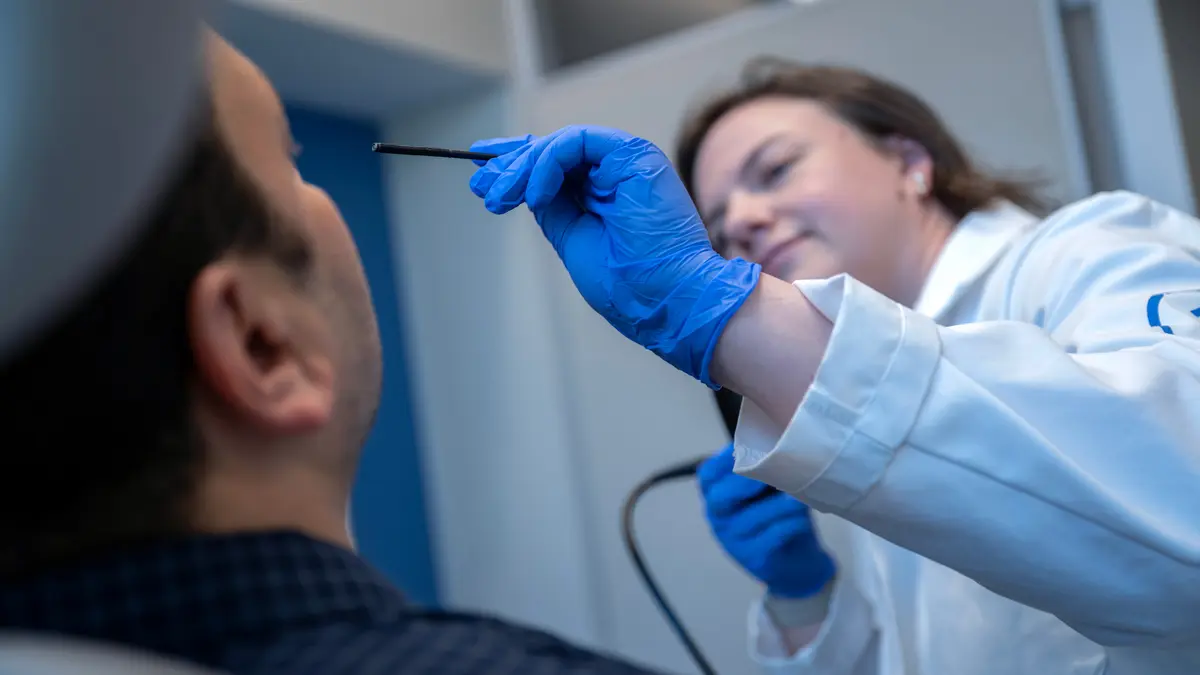 An MSK speech pathologist holds a fiberoptic endoscope near a patient’s head to examine him. 