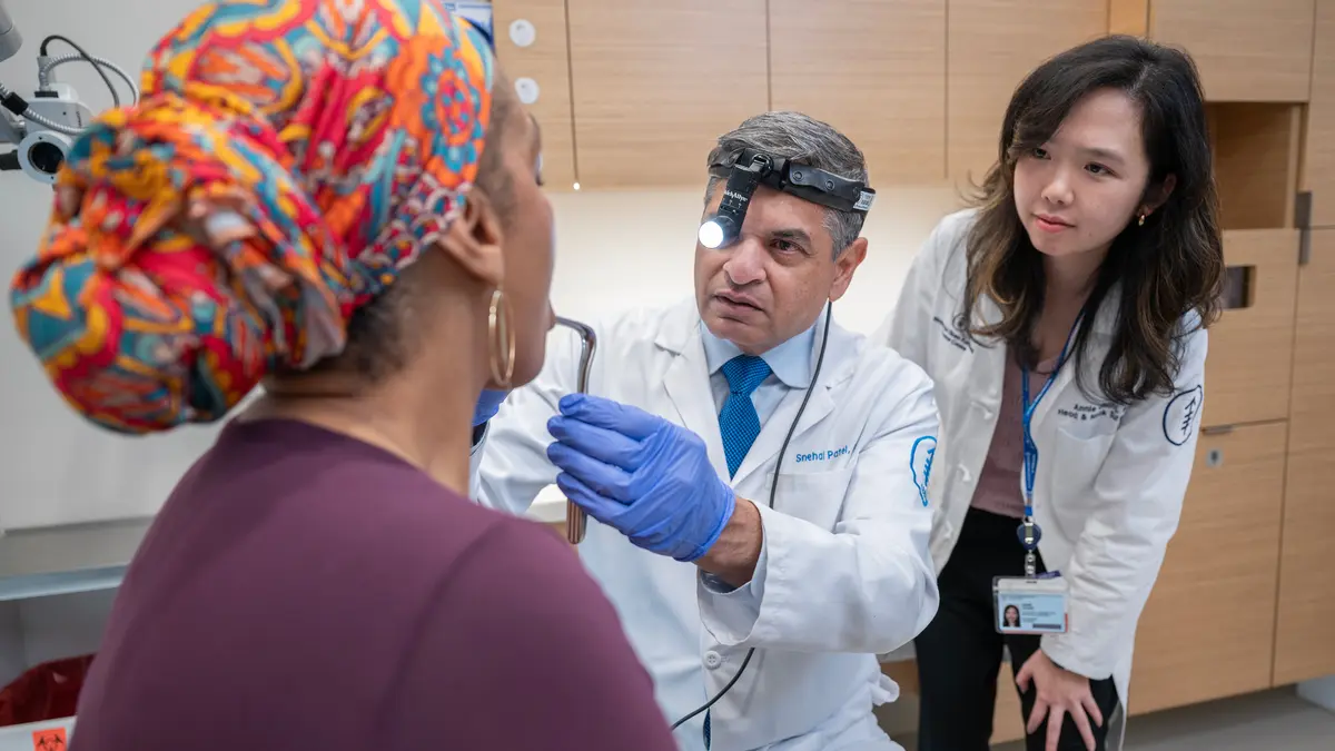 Head and neck surgeon Dr. Snehal G. Patel examines a patient, with physician assistant Annie Chang standing behind him and watching. 
