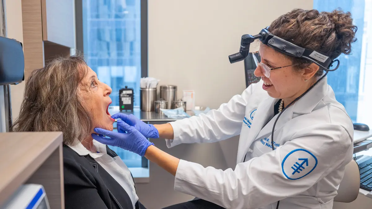 In an exam room, head and neck surgeon Dr. Jennifer Cracchiolo examines the mouth of her MSK patient with gloved hands.  
