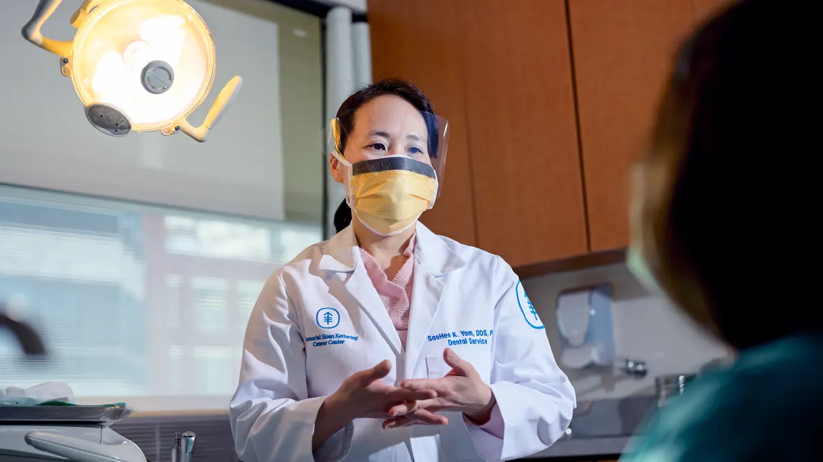 A masked MSK dental oncologist talks with her patient in an MSK exam room. 