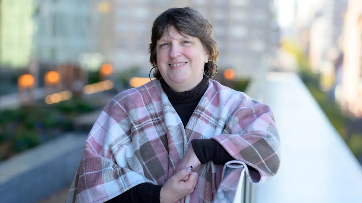 Person smiling on an outdoor terrace while wearing a pink plaid shawl.